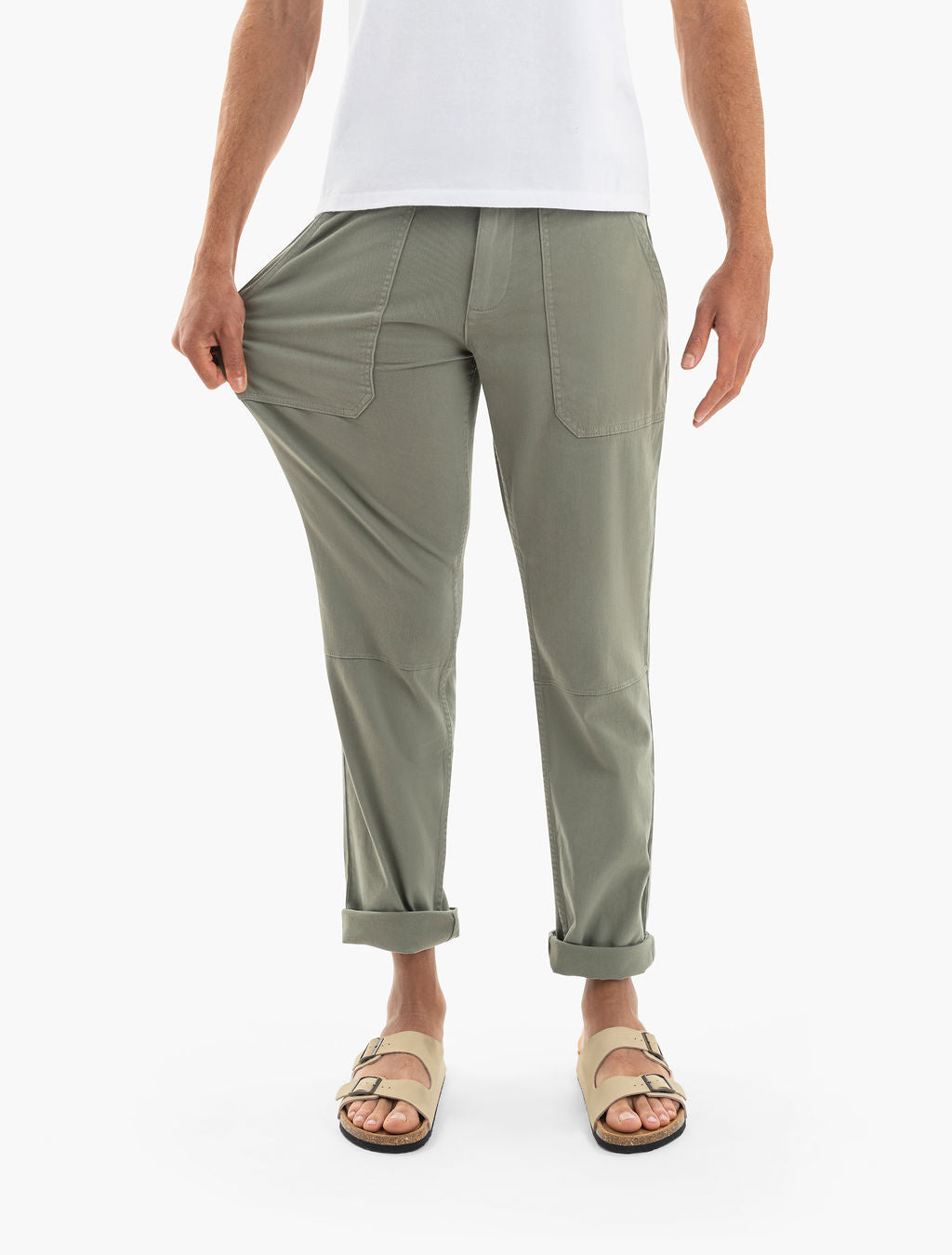 Model wearing olive-green rolled-cuff utility pants with front patch pockets and beige buckle sandals