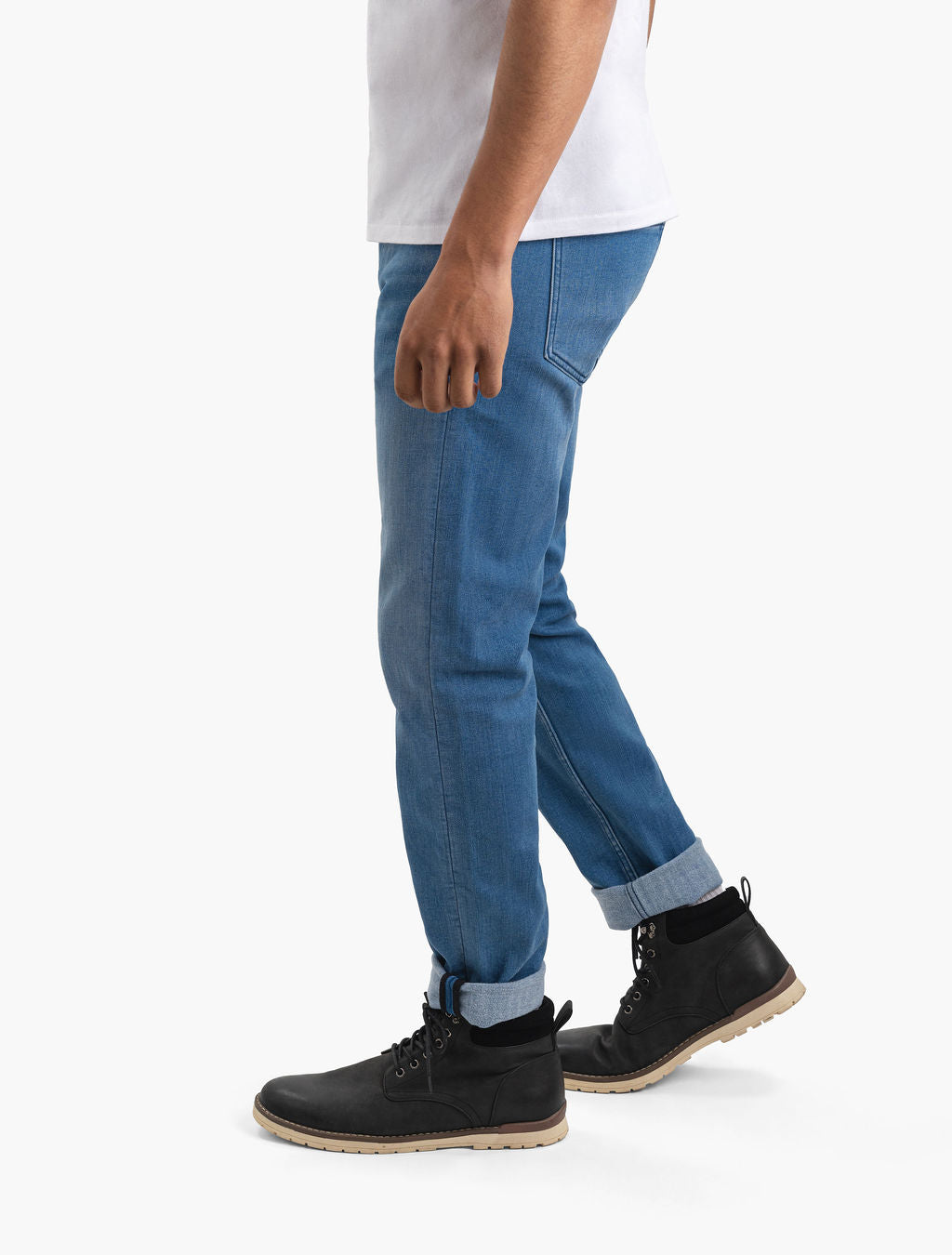 Person wearing cuffed blue jeans and black lace-up boots, shown waist-down, walking