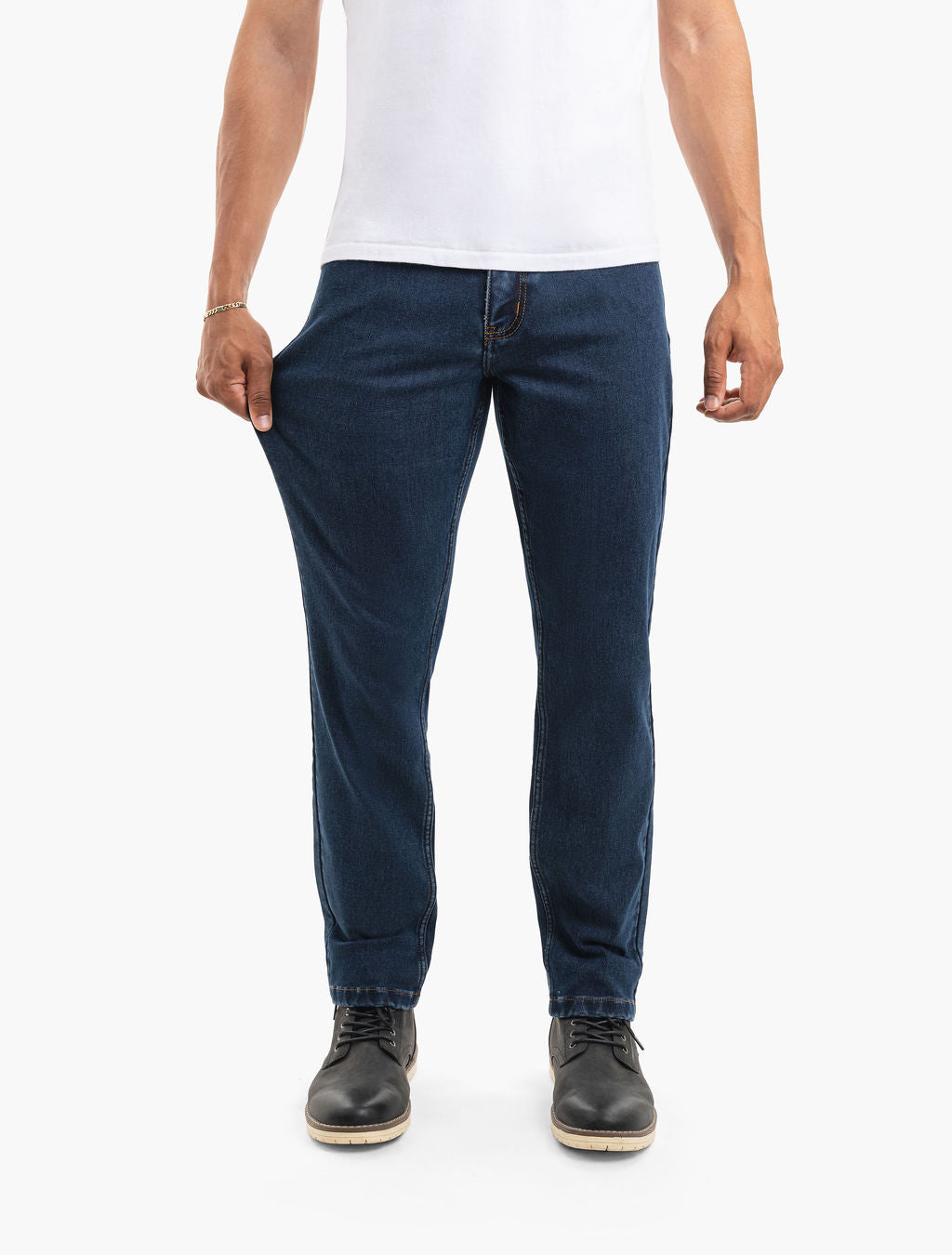 Men's dark indigo stretch jeans shown on model, pulling thigh fabric to demonstrate stretch and fit, with boots visible.