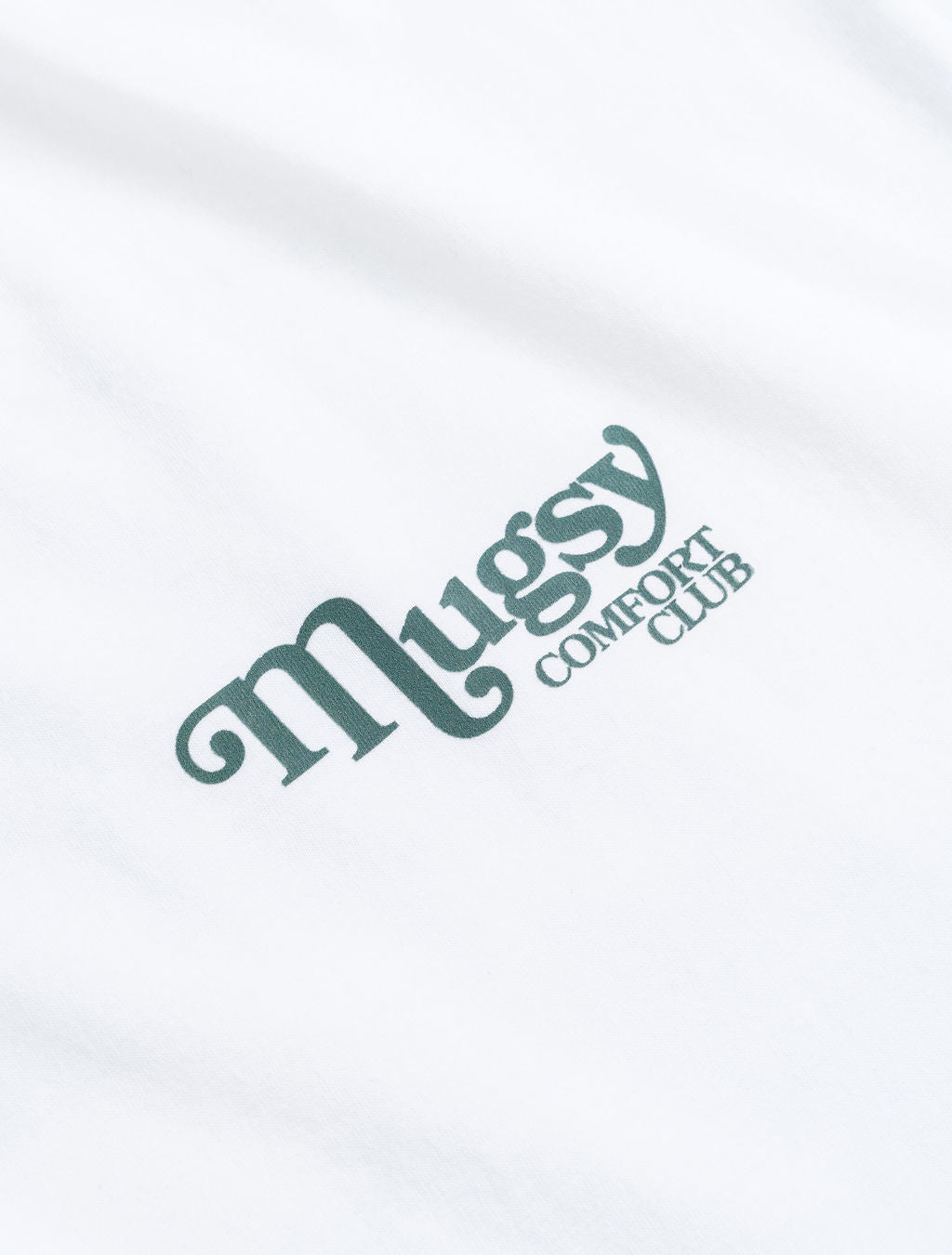 Close-up of white tee with green 'Mugsy' logo and smaller 'COMFORT CLUB' text