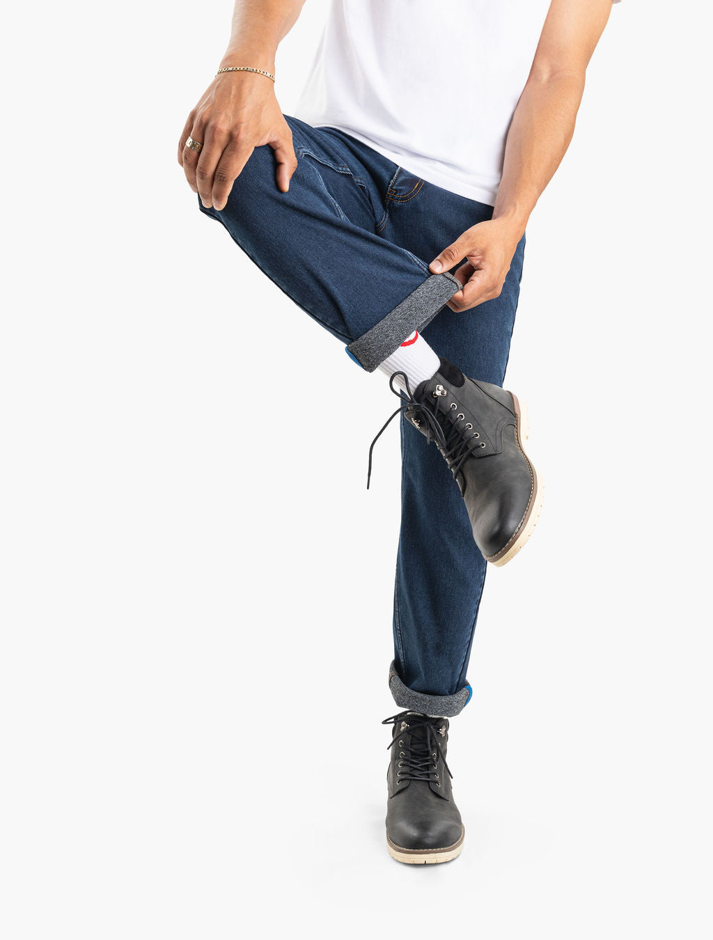 Person rolling up a dark blue denim pant cuff to reveal a white sock and black leather lace-up boot.