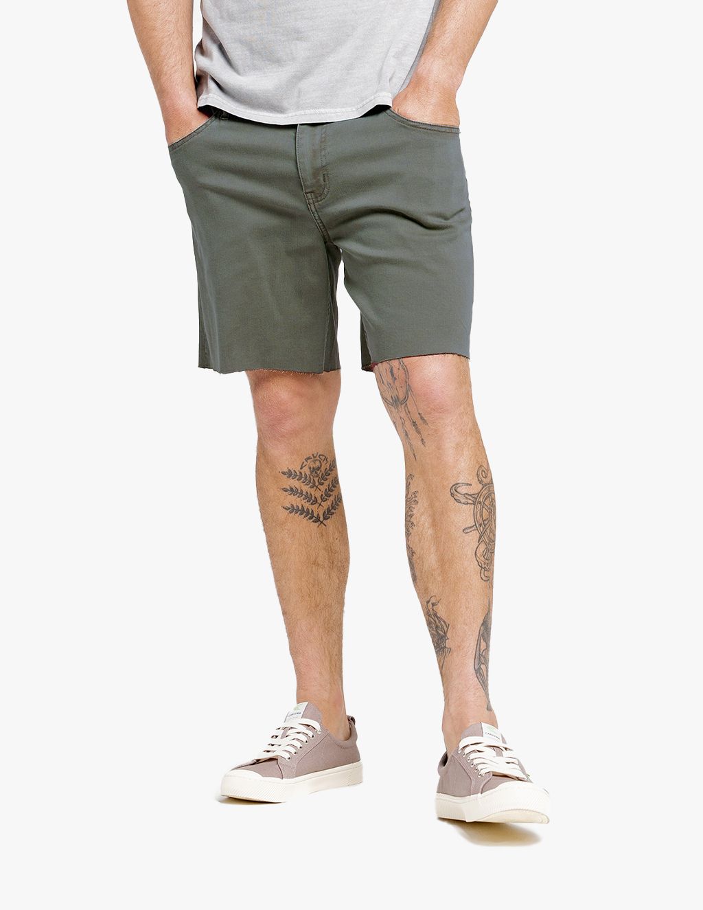 Man wearing olive green shorts and beige casual shoes, standing with hands in pockets.