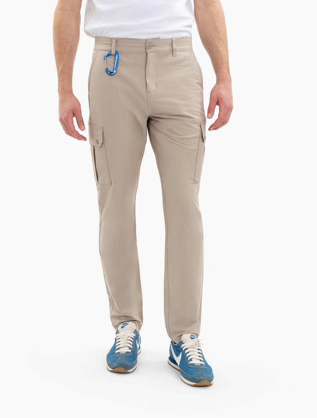 Men's beige cargo pants with flap pockets and blue carabiner on belt loop; model wearing blue NIKE sneakers.