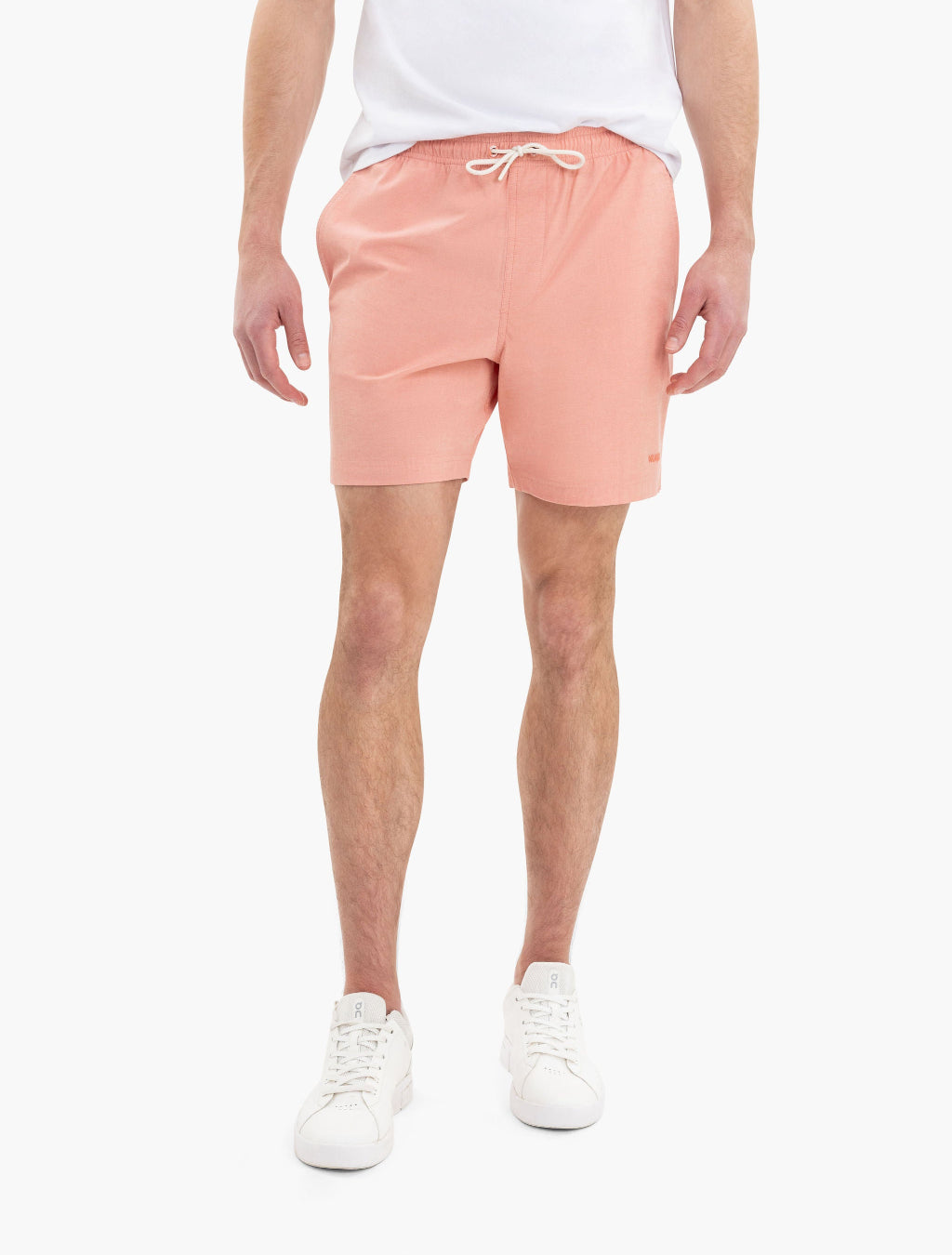 Man wearing salmon-colored shorts with drawstring and white sneakers, shown from waist to feet against a white background