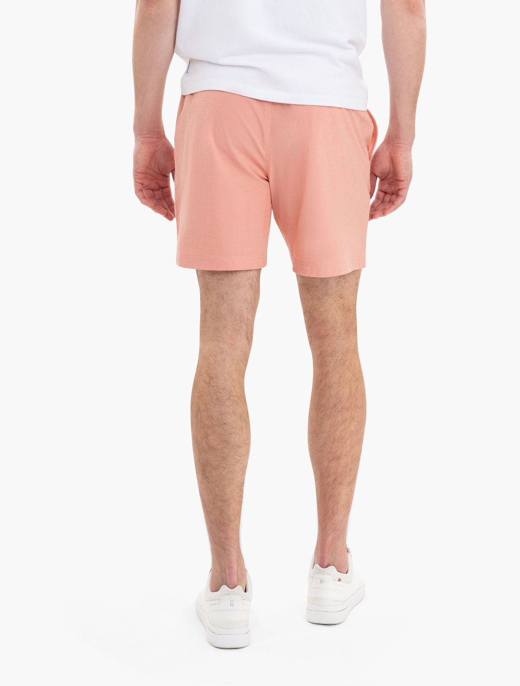 Back view of a person wearing peach shorts and white sneakers, standing against a white background.