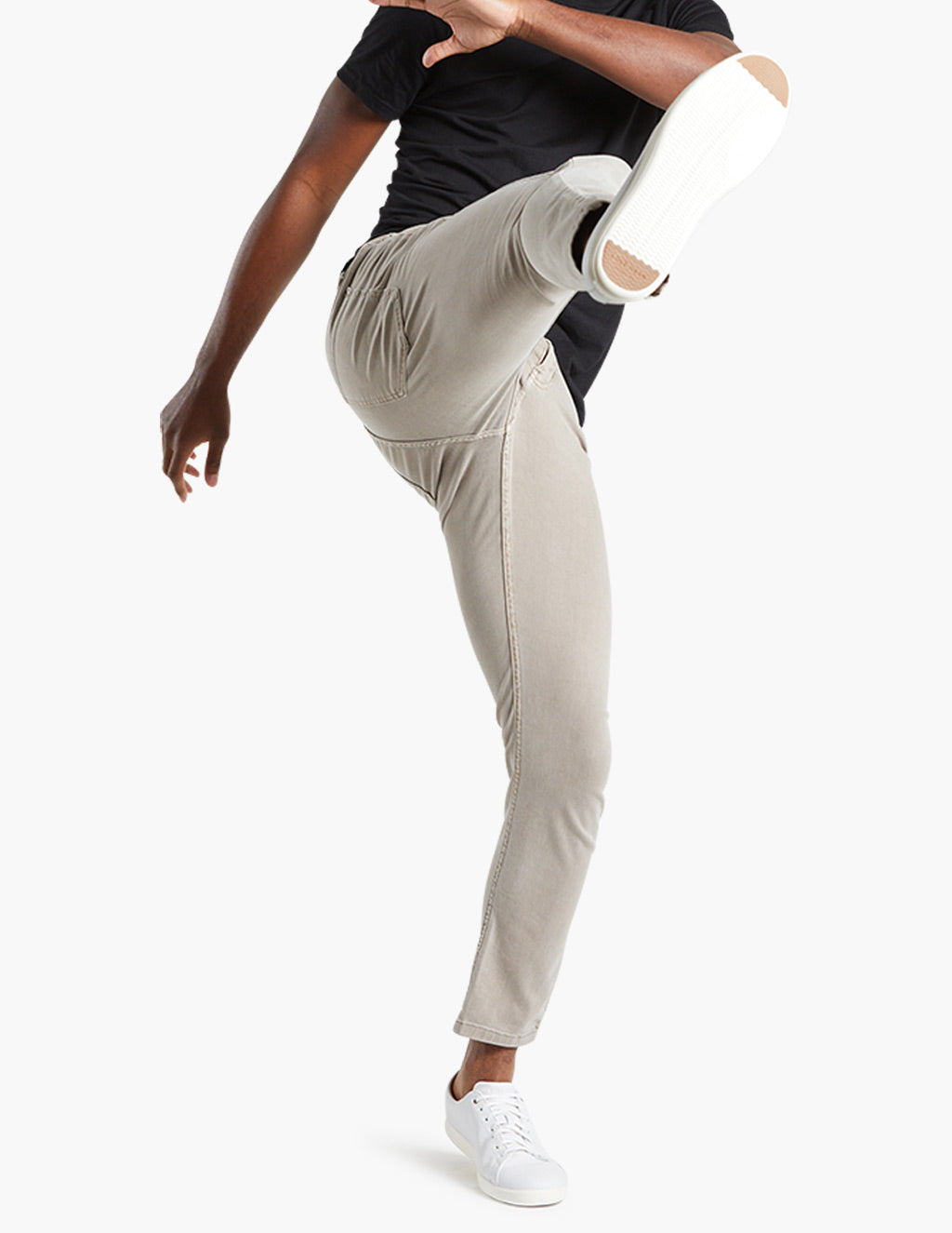 Person in beige slim-fit pants and white sneakers raising leg in mid-kick, cropped above waist