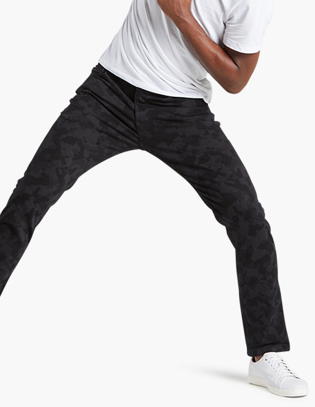 Person wearing black camouflage pants and white sneakers, cropped torso and legs in wide stance