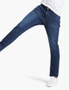 Person wearing dark blue jeans and white sneakers, with one leg raised mid-step.