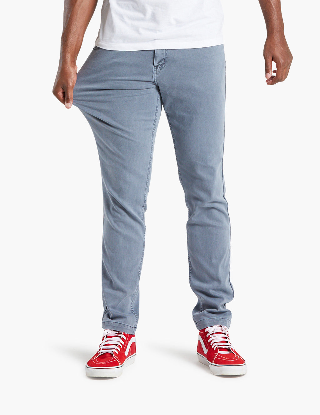 Men's light-blue slim stretch pants on model pulling thigh to show stretch; red sneakers visible
