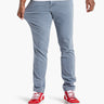 Men's light-blue slim stretch pants on model pulling thigh to show stretch; red sneakers visible