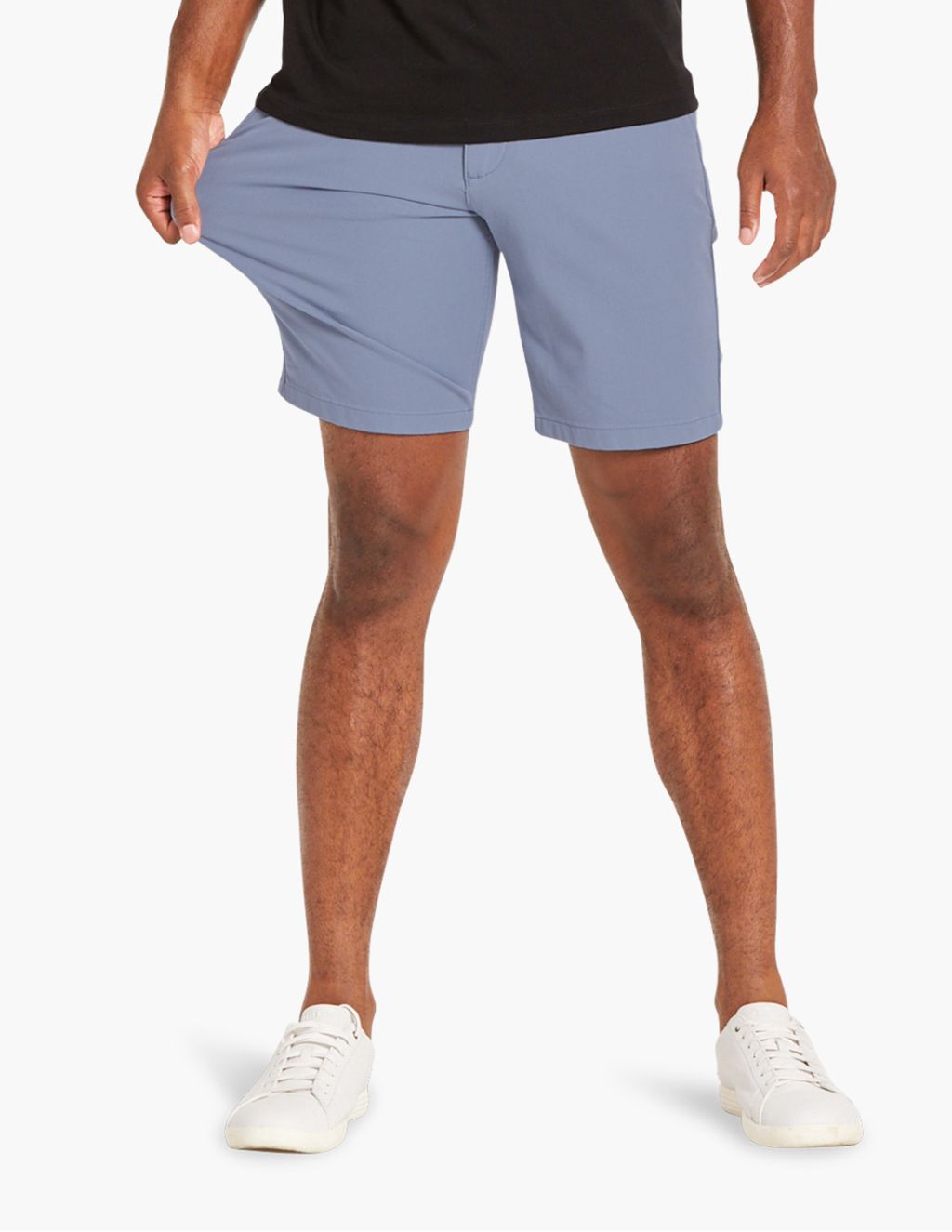 Man wearing light blue shorts and white sneakers, cropped at the waist