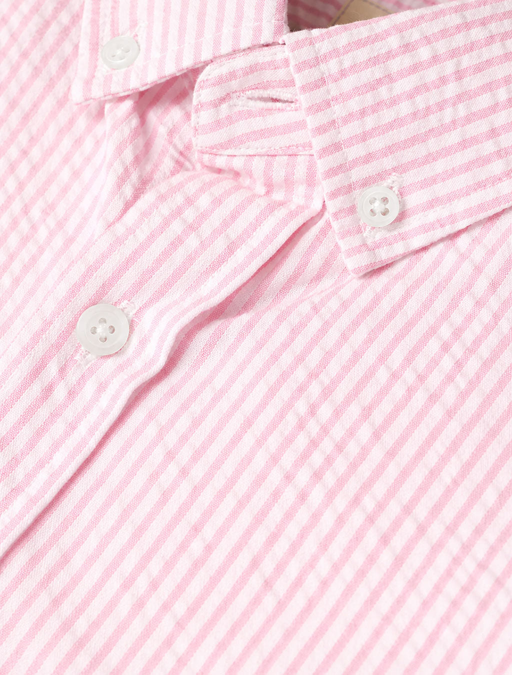 Close-up of pink seersucker short-sleeve shirt collar and front placket showing narrow pink-and-white stripes, textured fabric, and white buttons