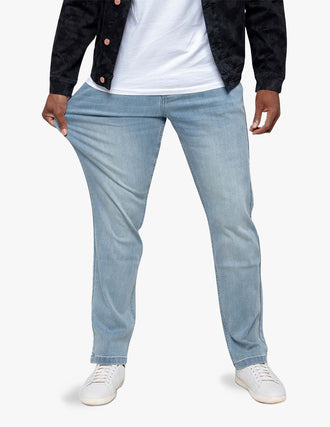 Man wearing light-wash relaxed-fit jeans, holding fabric at thigh to show stretch; white sneakers visible