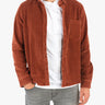 Male torso wearing open rust corduroy shirt over white T-shirt and faded gray jeans, hands partially in pockets.