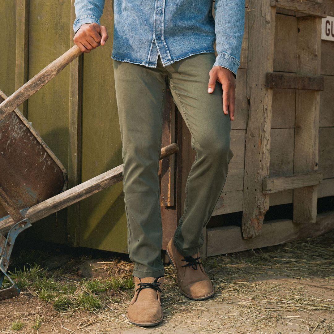 Front view of Rangers pants on model showcasing olive green slim fit with tan suede boots and rustic shed background