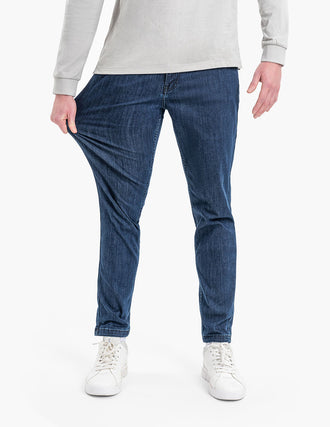 Blue tapered men's jeans, model pulling thigh to show stretch and slim fit.