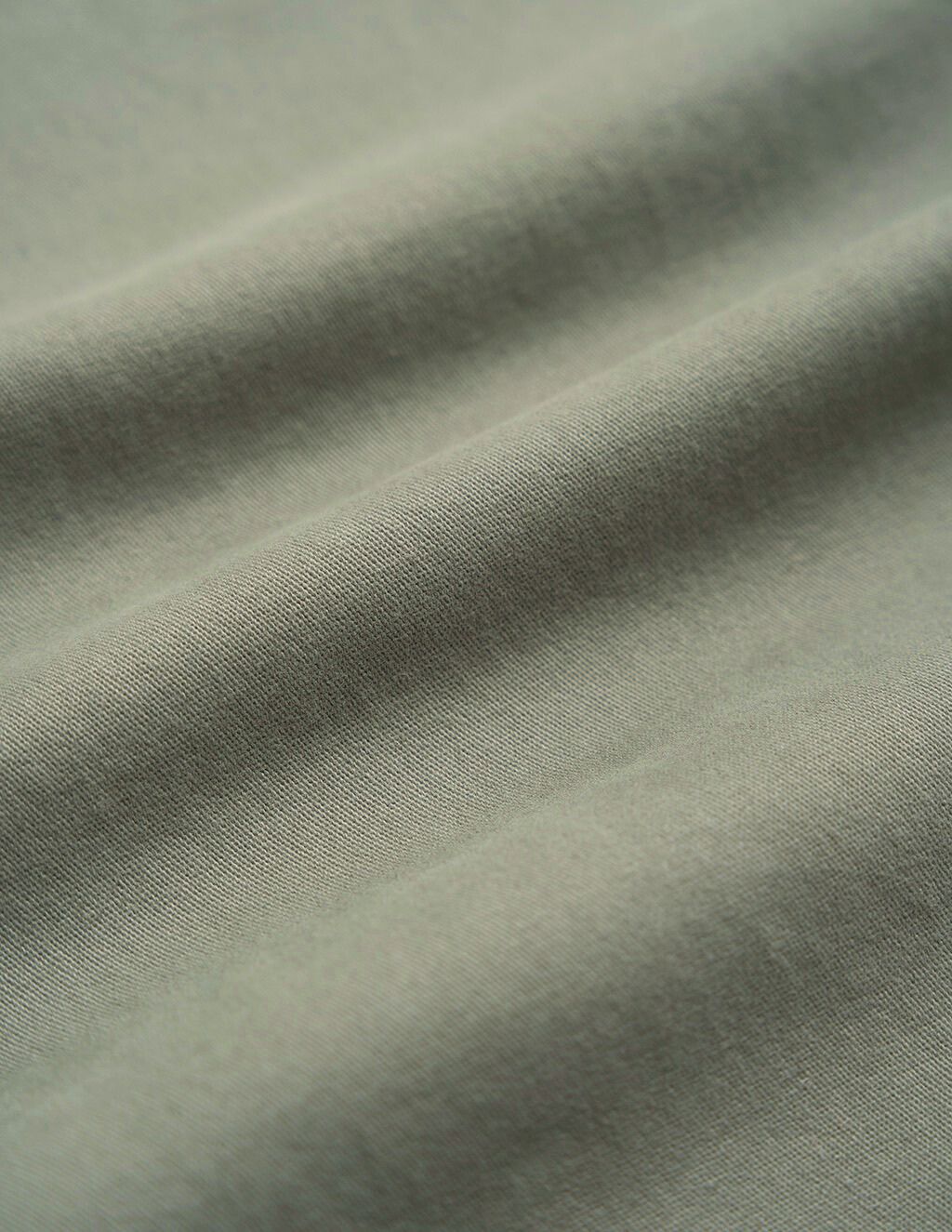 Olive-green cotton fabric close-up showing soft diagonal folds and fine knit texture