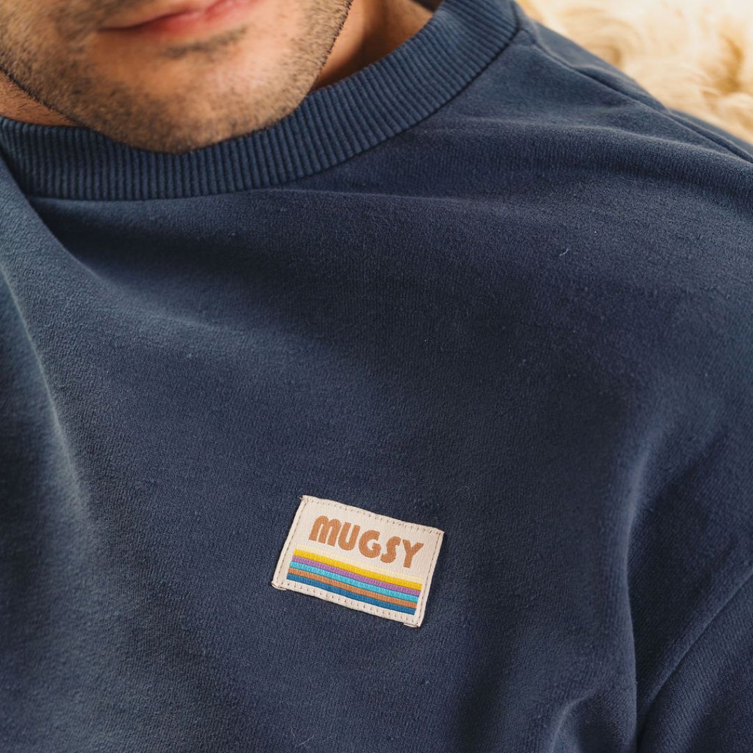 Navy sweatshirt chest patch reading MUGSY above multicolored horizontal stripes.