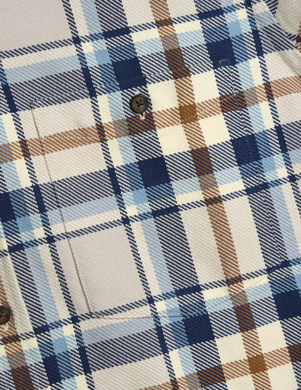Close-up of blue, cream and brown plaid shirt fabric showing button and pocket seam.