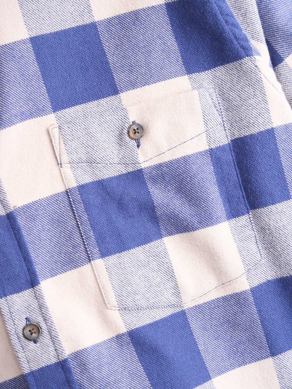 Close-up of blue and cream buffalo-plaid flannel shirt pocket showing button and stitched pocket detail.