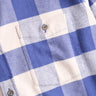 Close-up of blue and cream buffalo-plaid flannel shirt pocket showing button and stitched pocket detail.