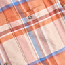 Close-up of orange, blue and cream plaid flannel shirt showing a chest pocket and two brown buttons