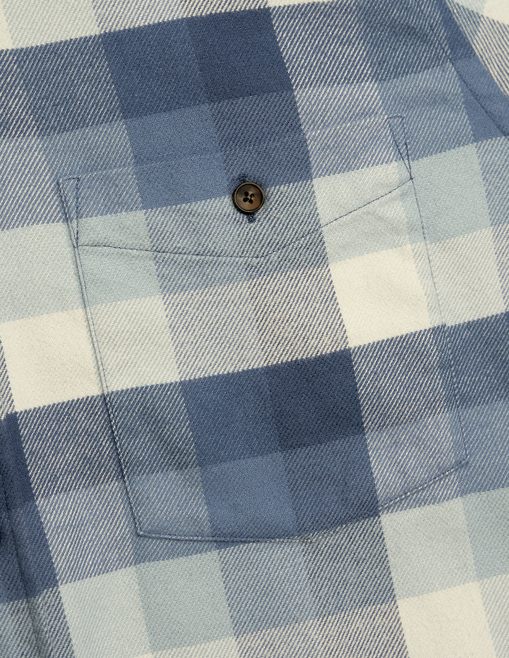 Close-up of blue and white plaid shirt pocket with single brown four-hole button and visible stitching.