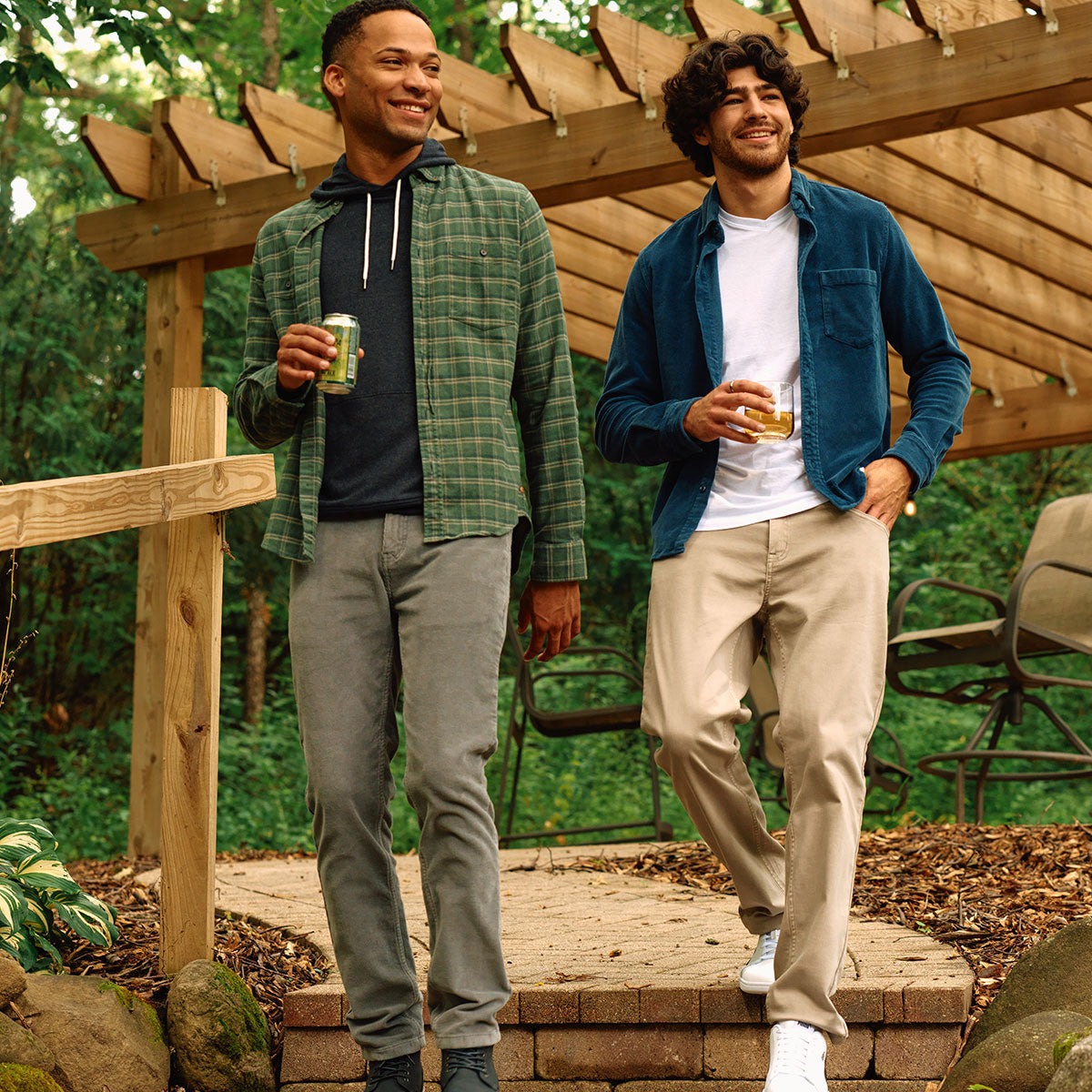 Two men in casual outfits, one in a green plaid shirt and the other in a blue jacket, holding drinks on a wooden deck.