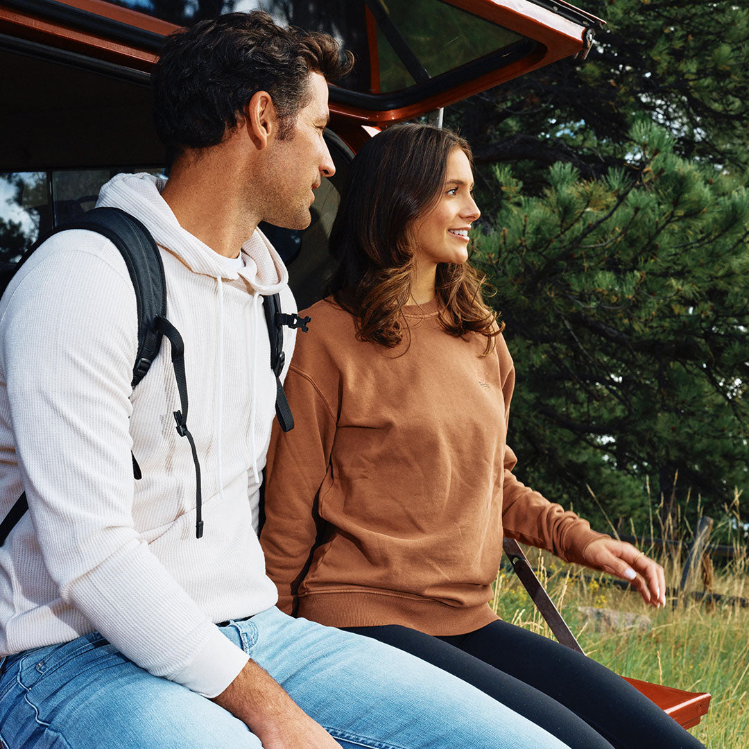 A man and woman sitting outdoors, wearing casual hoodies and jeans, enjoying nature.