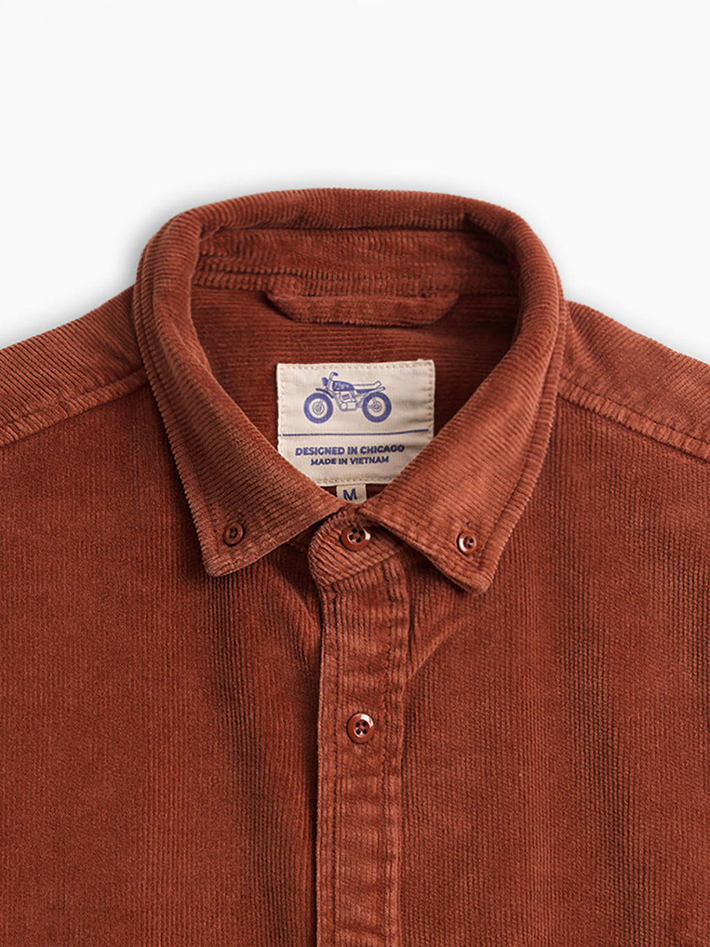 Rust corduroy button-down shirt collar with label reading 'DESIGNED IN CHICAGO MADE IN VIETNAM M' and motorcycle logo