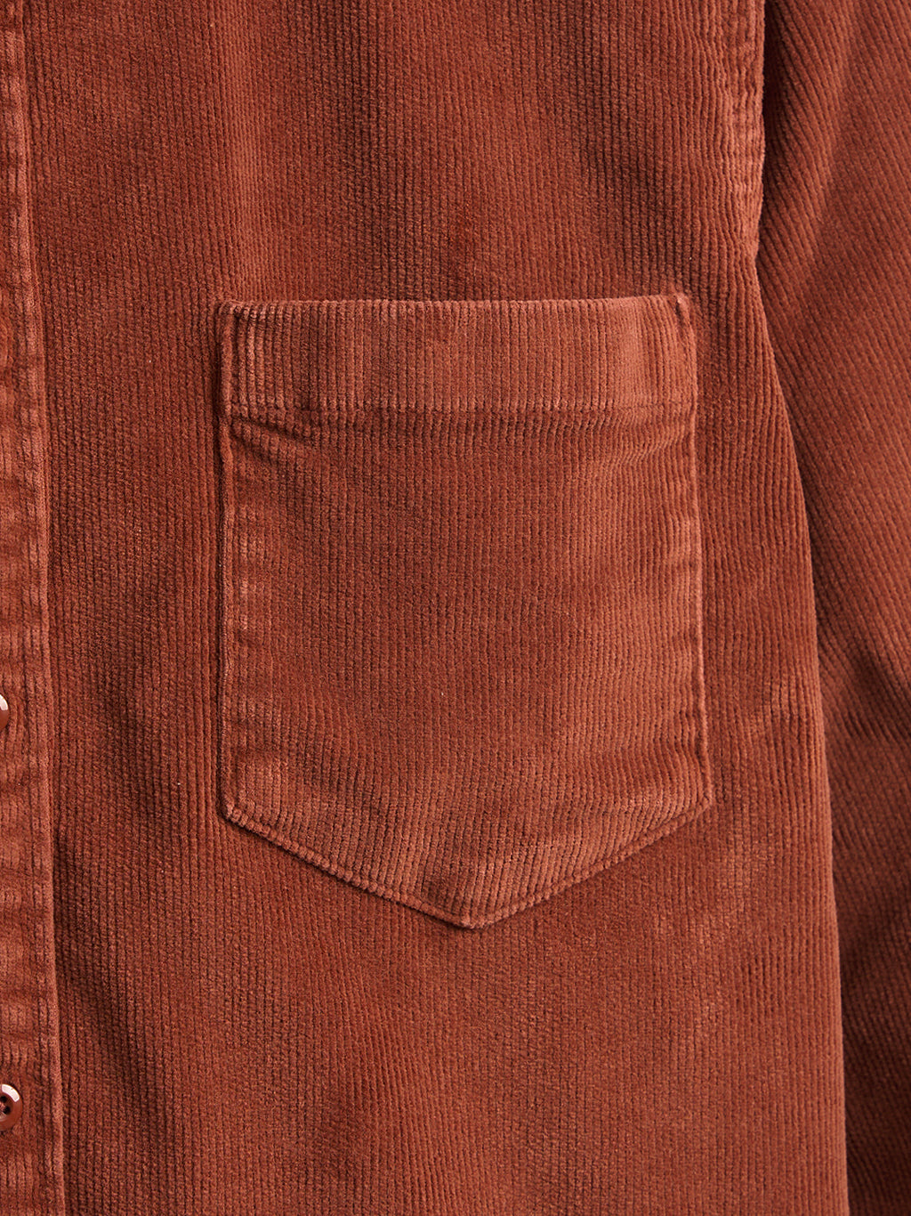 Rust corduroy jacket front pocket and vertical ribbed fabric texture.