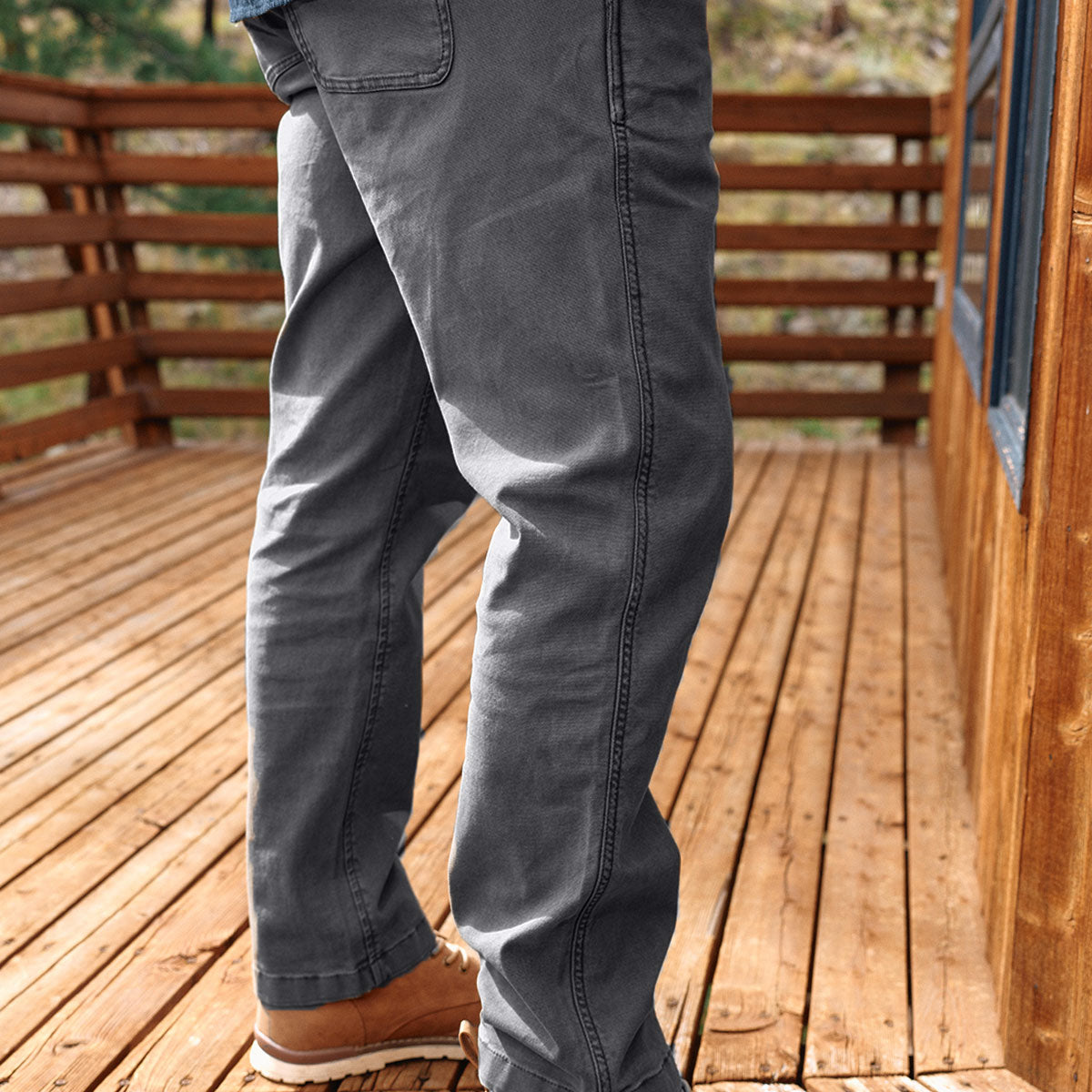 Lower legs in gray pants and brown boots standing on a wooden deck beside a cabin wall.