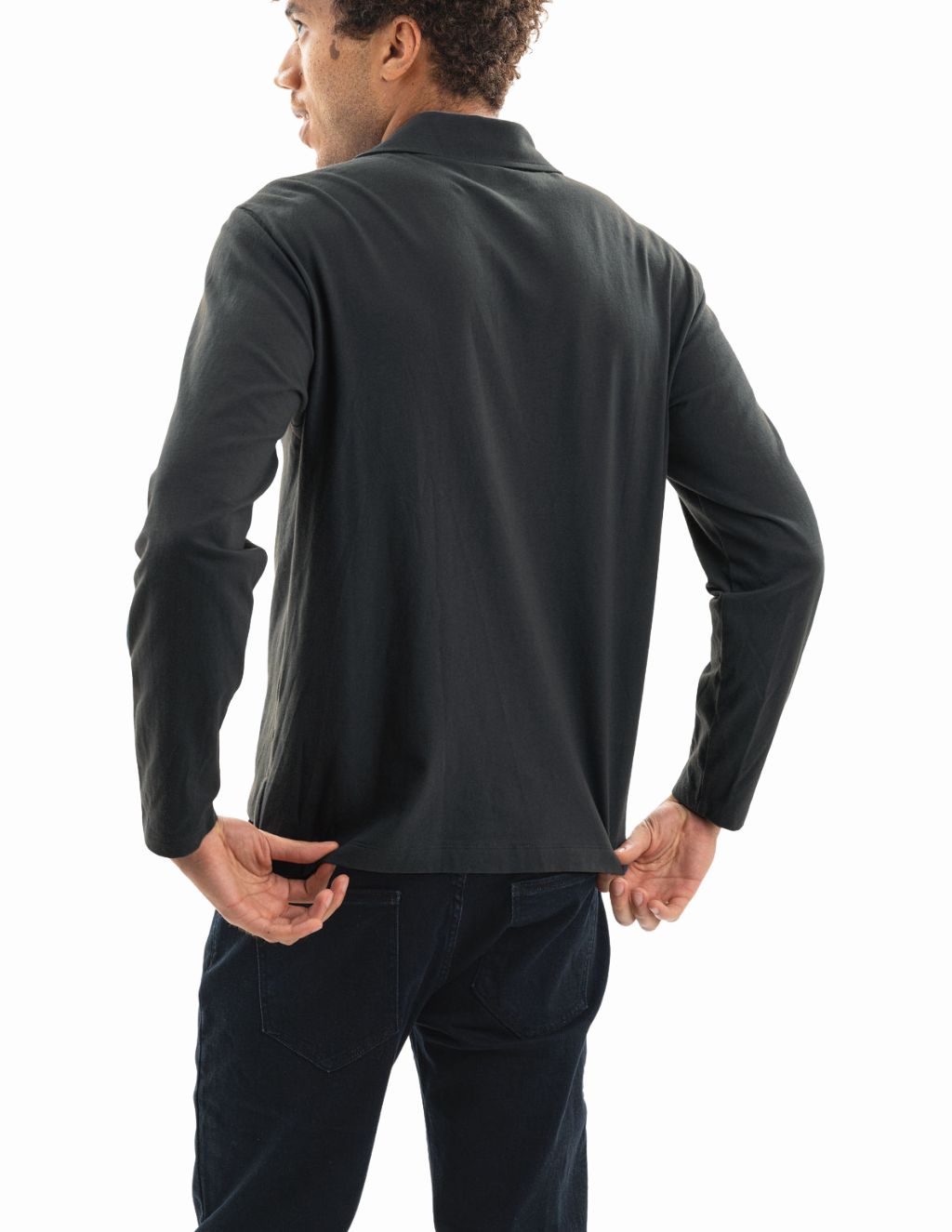 Rear view of a man wearing a dark long-sleeve polo shirt pulling down the hem