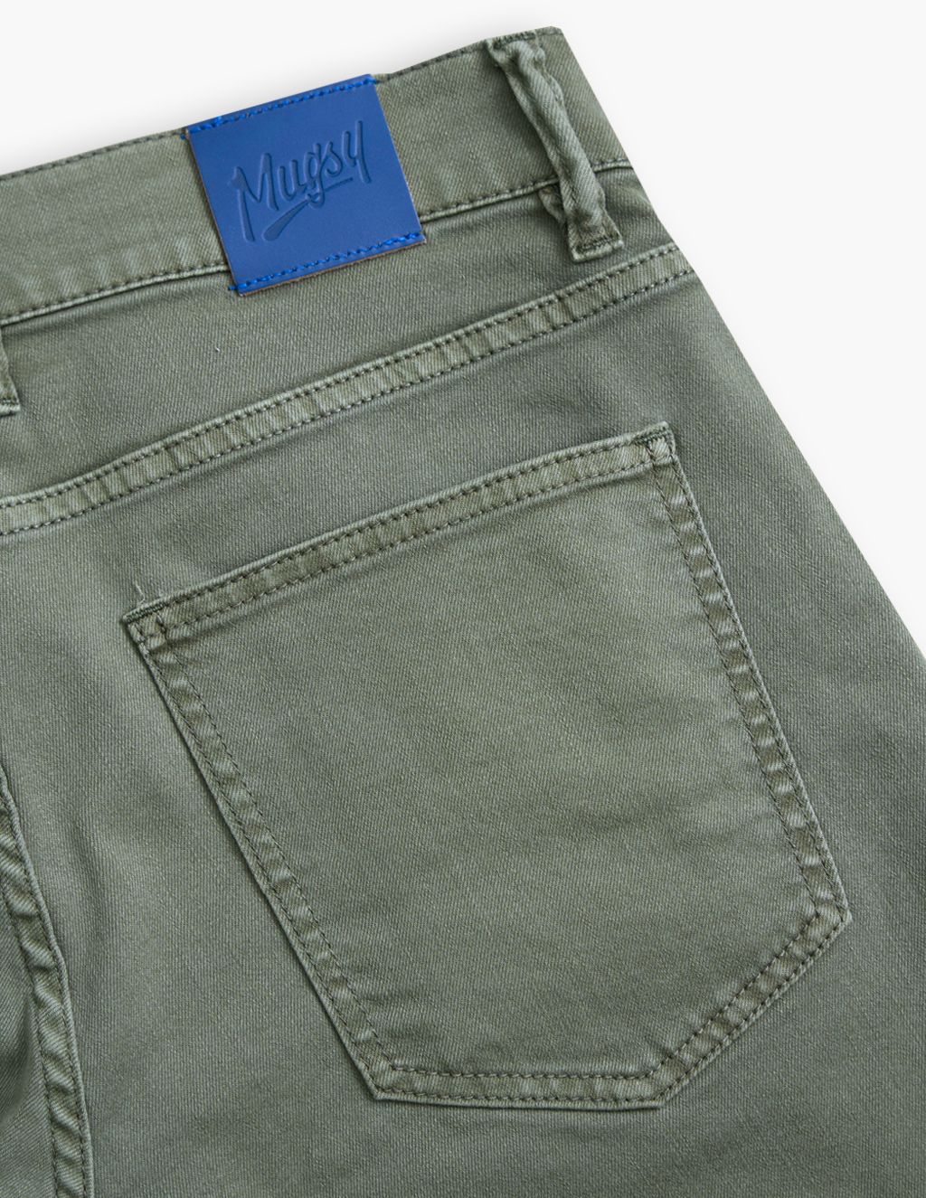 Close-up of the back pocket of green pants with a blue label reading 'Mugsy'