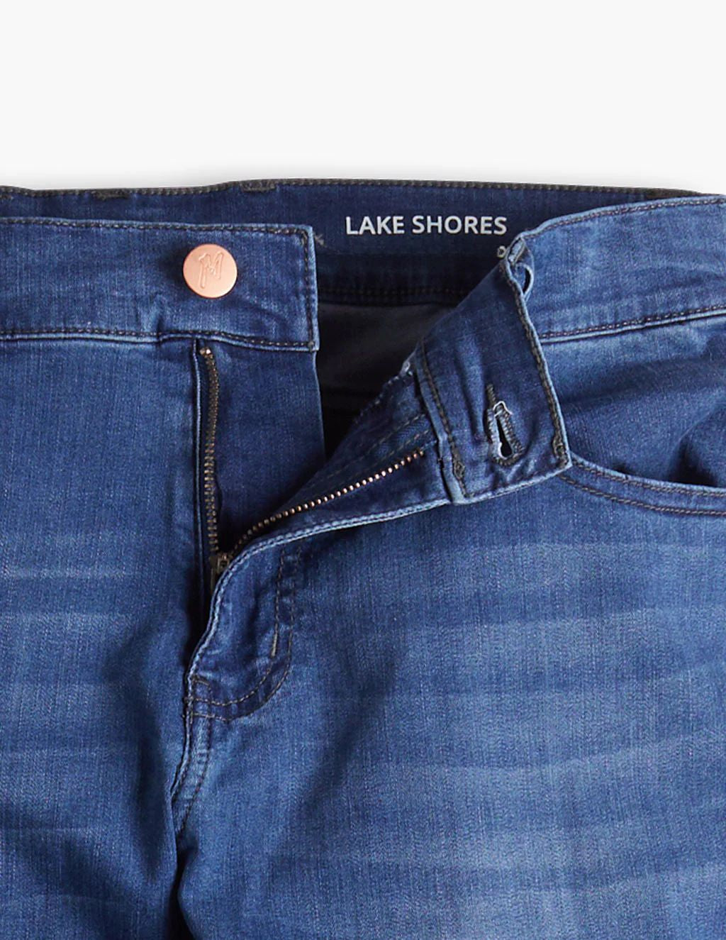 Blue denim jeans waistband with open zipper, button marked 'M' and inner label reading 'LAKE SHORES'.