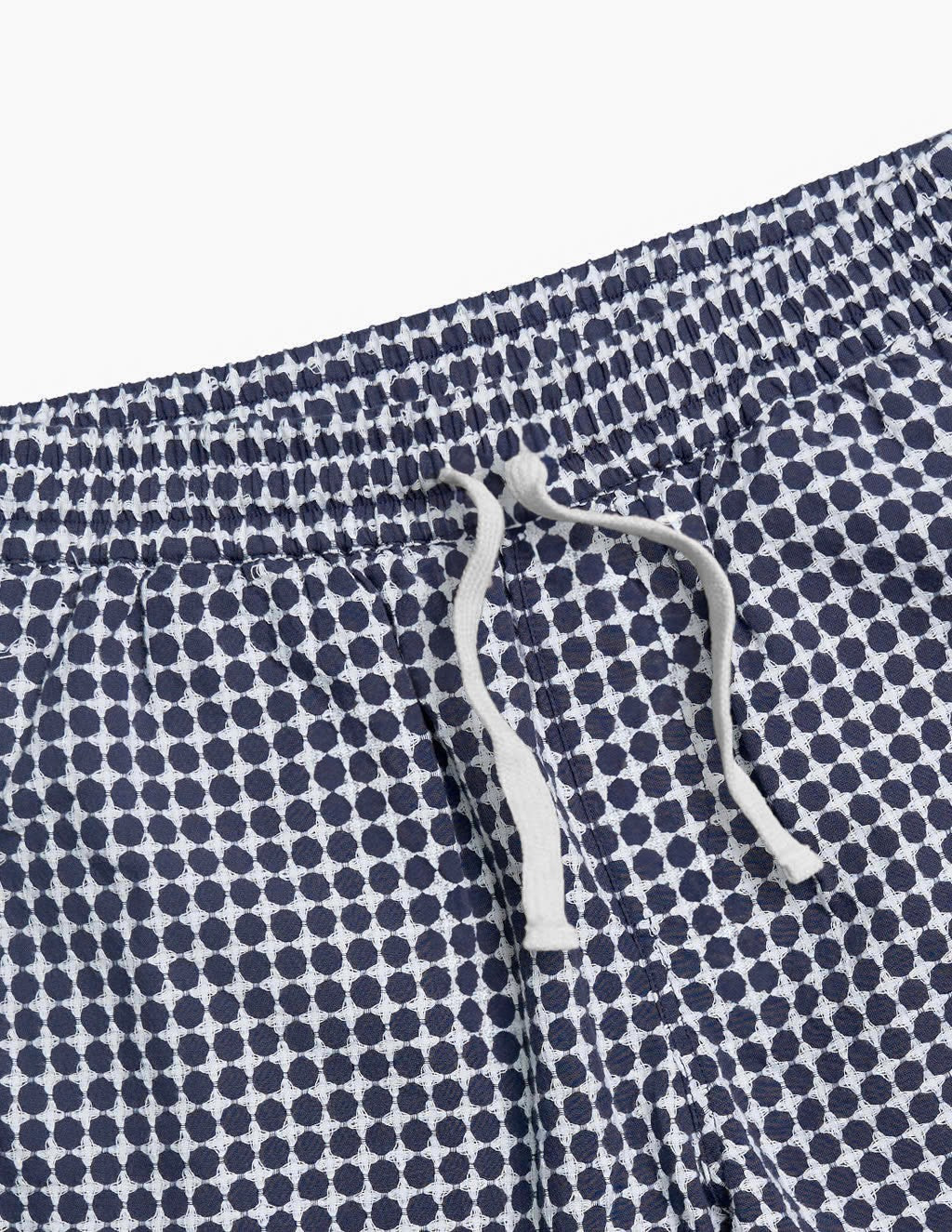 Close-up of navy blue and white patterned swim shorts with a white drawstring tied in a loose knot.