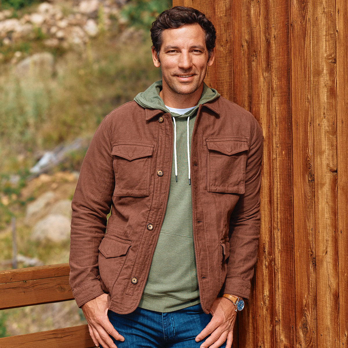 Man in a brown jacket and green hoodie standing outdoors