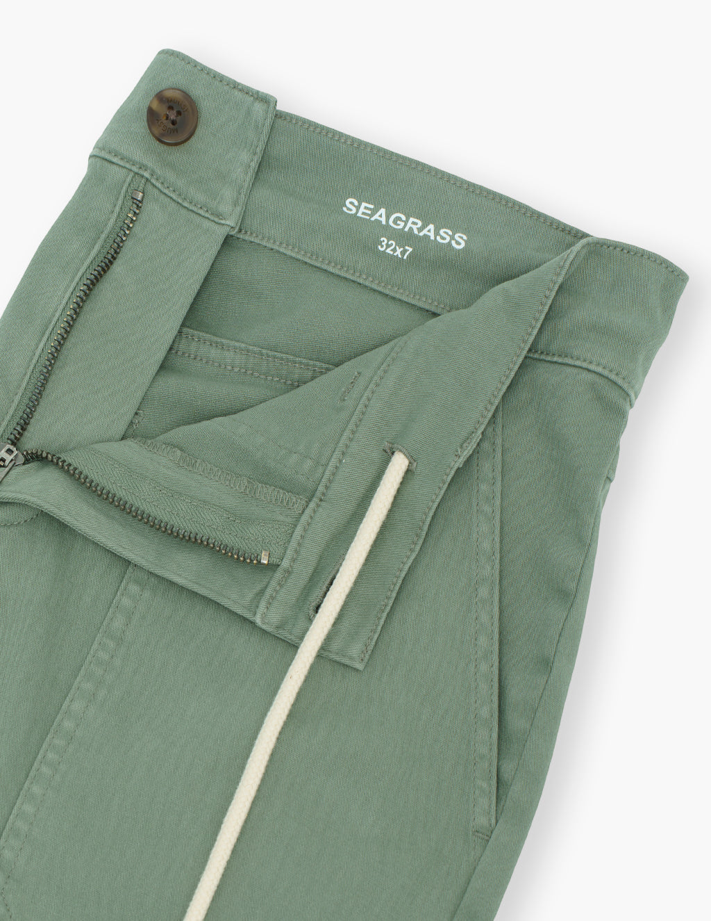 Close-up of Seagrass drawstring shorts waistband with zipper, button, drawstring, and interior label SEAGRASS 32x7 on white