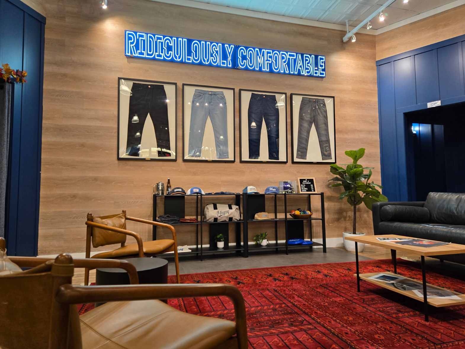 Retail lounge with leather chairs, framed jeans on a wood wall and neon sign reading 'RIDICULOUSLY COMFORTABLE'.