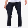 Men's dark indigo straight-fit jeans on model; hand stretching fabric to show stretch and fit