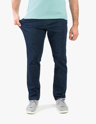 Model wearing dark blue casual stretch jeans, pulling left thigh to show fit; mint T-shirt hem and gray sneakers visible