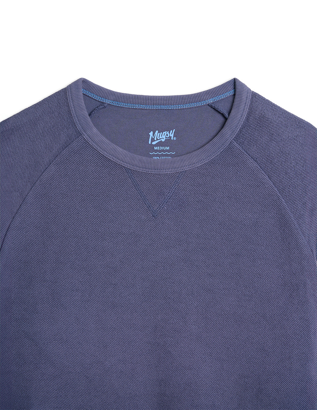 Close-up of indigo crewneck sweatshirt collar and upper front showing label 'Mugsy' MEDIUM 100% COTTON