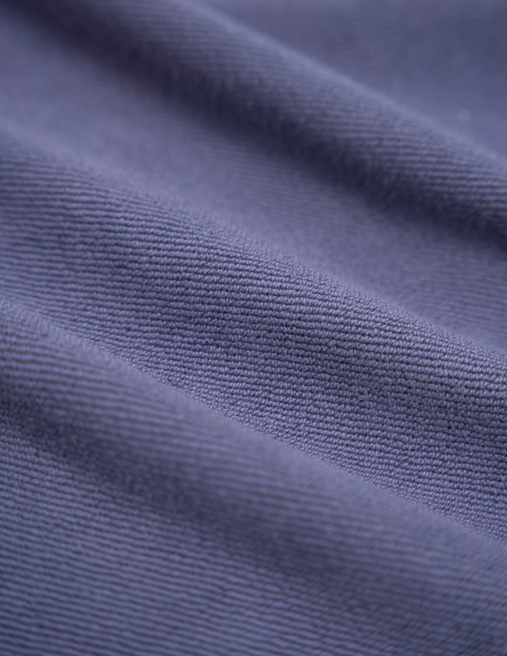 Close-up of purple-blue ribbed fabric showing textured knit and diagonal folds.
