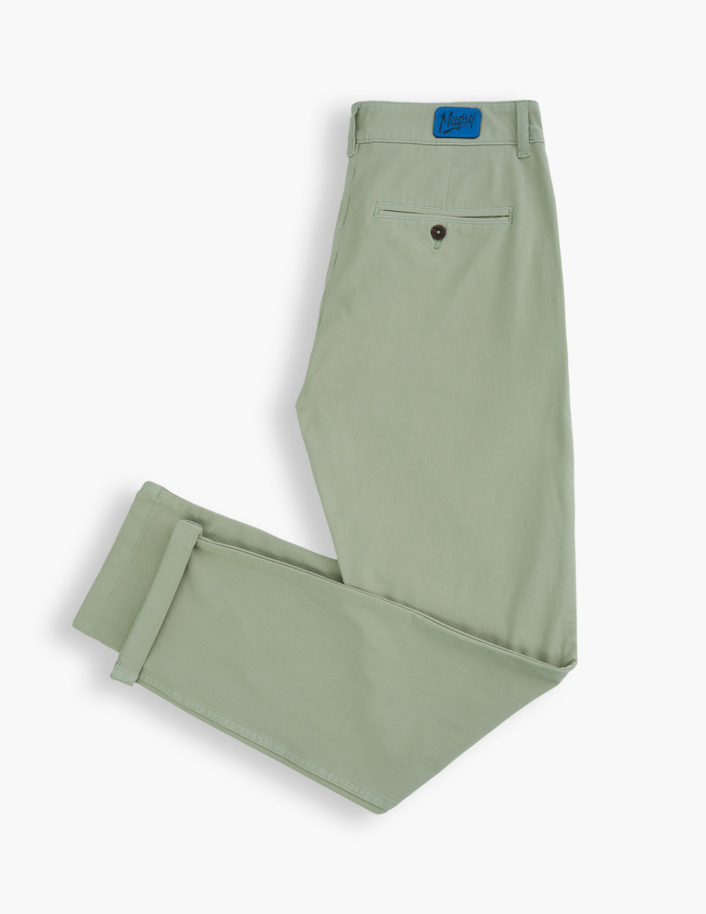 Flat lay of Willows chinos in sage green showing rear pocket, button detail, cuffed hem, and Mugsy patch on white background
