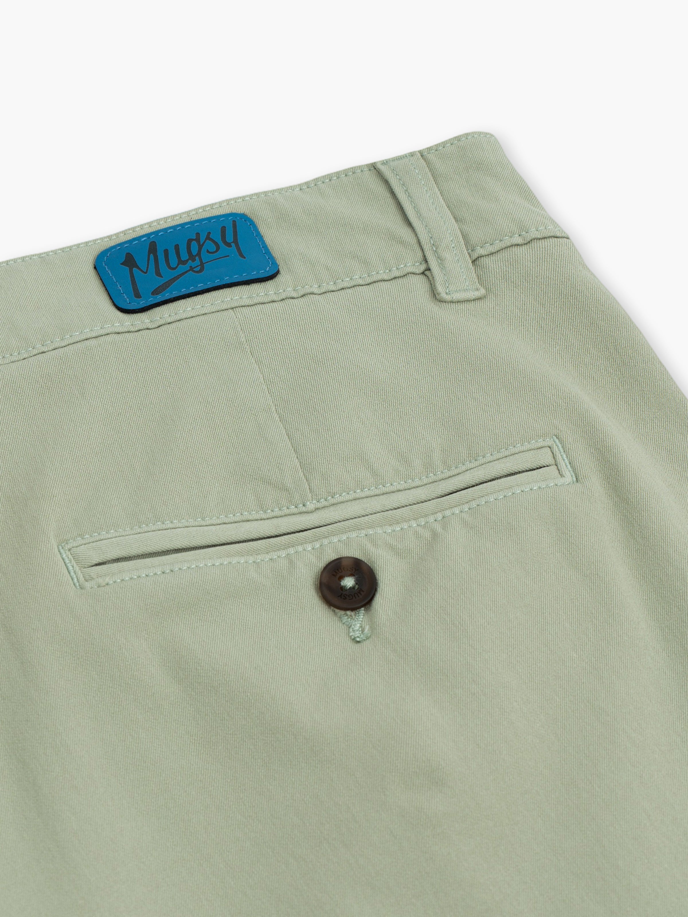 Back close up of Willows chinos in sage green showing welt pocket with button, belt loop, and blue Mugsy patch