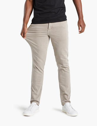 Front view of khaki jeans on model showcasing stretch as the model pulls the thigh area with white background
