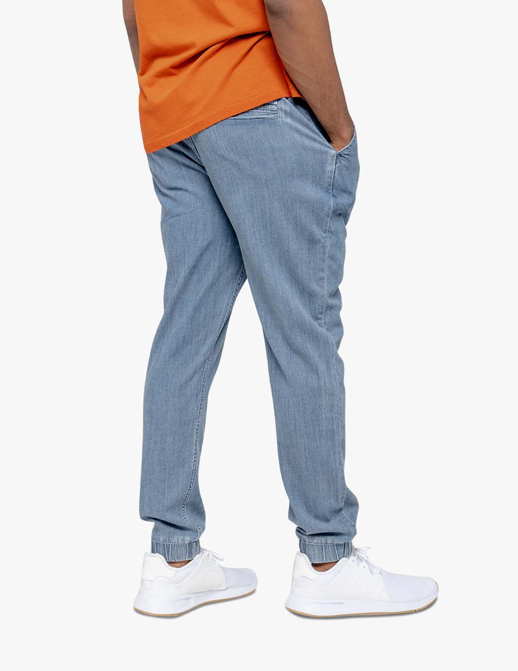 Men's blue stretch denim joggers with elastic cuffs, worn with a casual orange shirt.