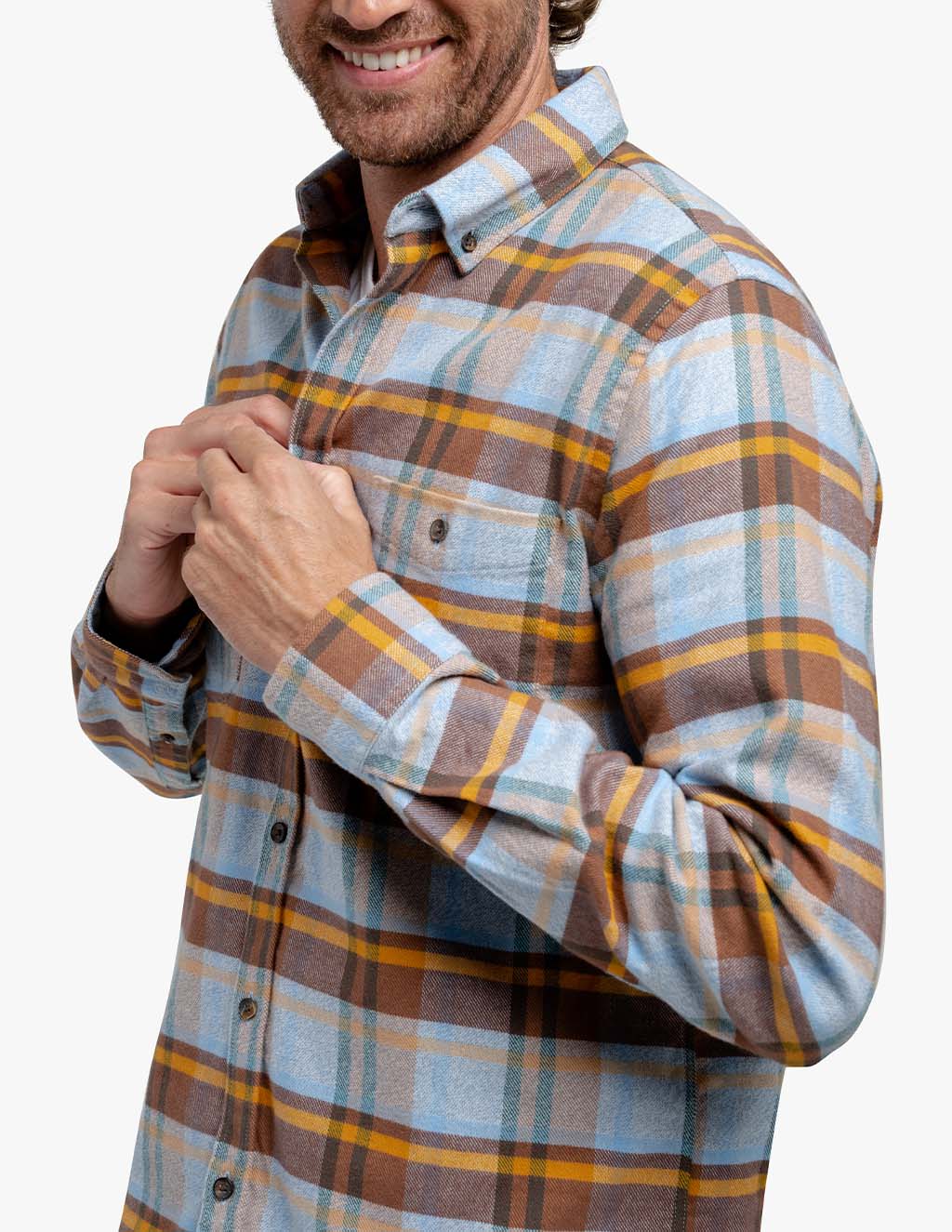 A man wearing a blue, brown, and gold plaid stretch flannel shirt, smiling and holding the shirt's front.
