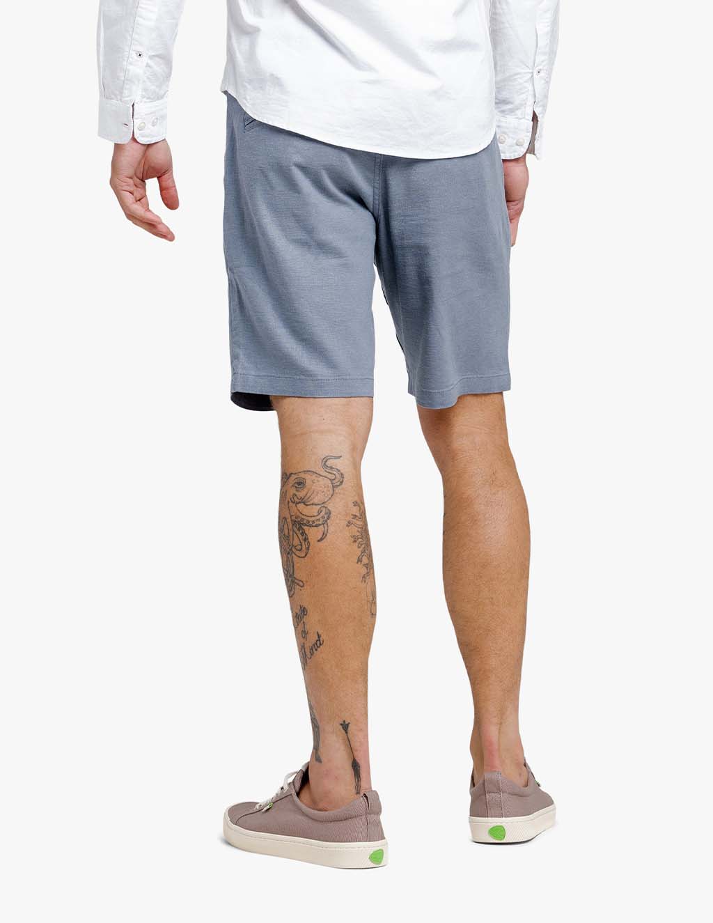 Man wearing comfortable blue stretch linen shorts from the back, showcasing tattoos and casual shoes.